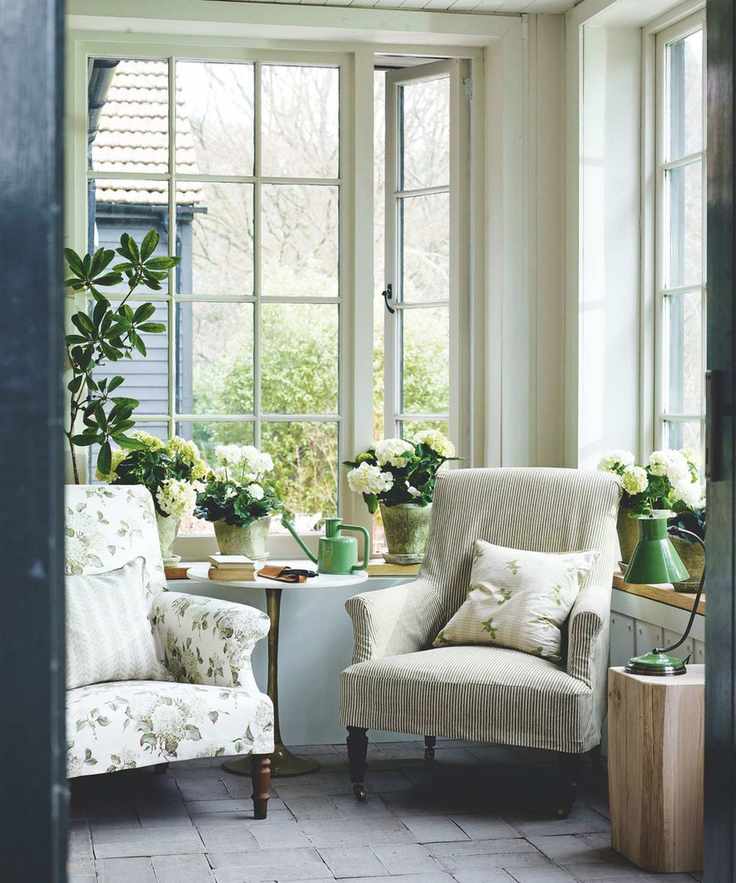 A bright and sunny sunroom with houseplants and mismatched armchairs.