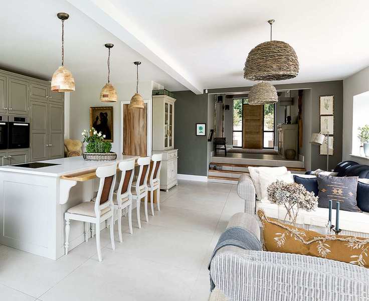 kitchen open plan with view of white wood edged island with painted wooden chairs and sofa and armchairs pale green cabinets and white tiled floor