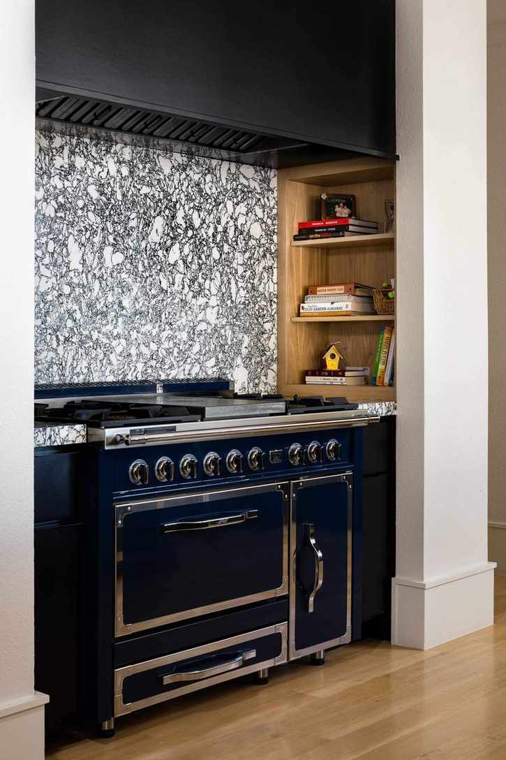 Stove with veined stone backsplash and niche with cookbooks