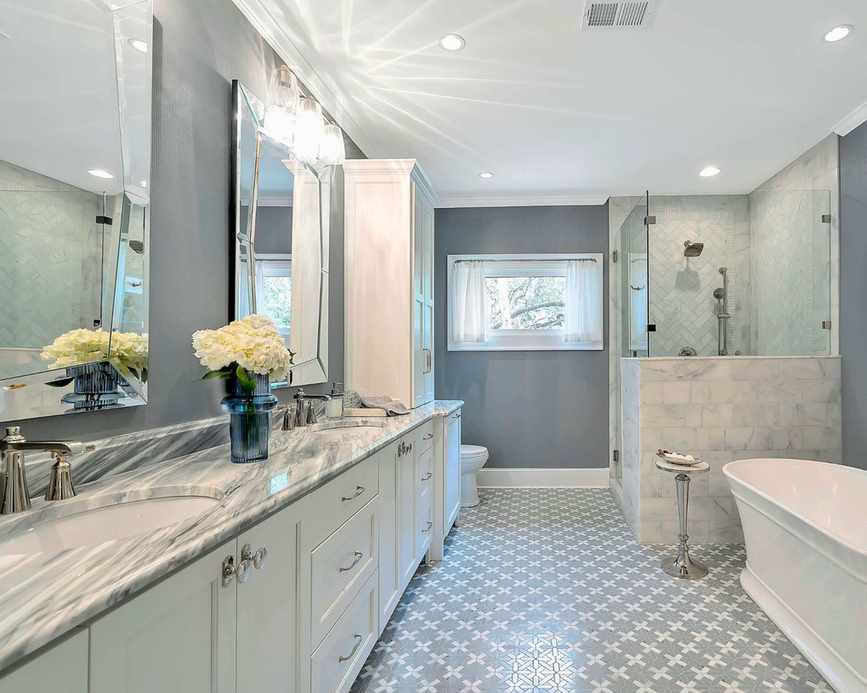 A large gray and white themed bathroom with long marble vanity, freestanding white tub, large walk in shower and mixed tiles