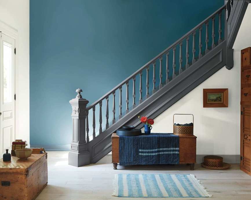 A hallway with a staircase leading upstairs. The wall is painted in a muted blue.