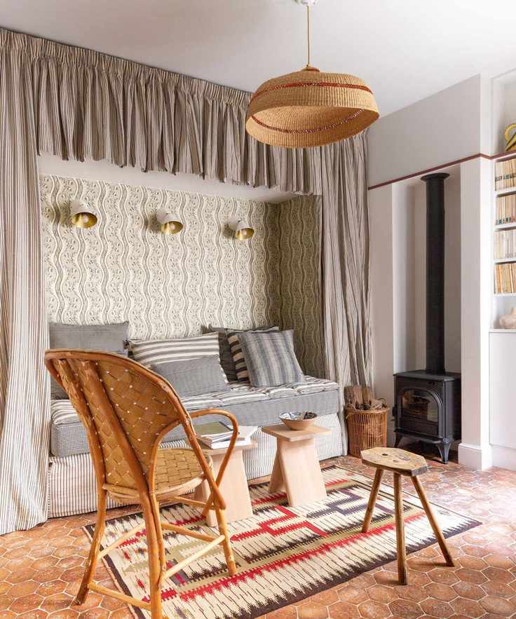 Bedroom with tiled floor, built-in bed niche with curtains and wallpaper, rattan armchair and wood side table and pendant light