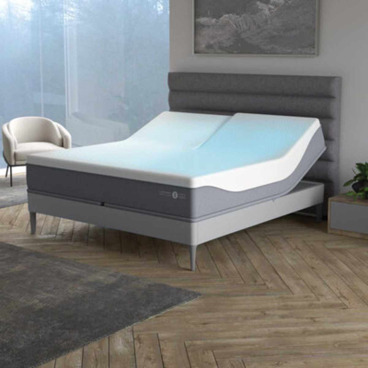 A grey fluted Sleep Number ClimateCool® smart bed in a neutral bedroom with white walls, wooden flooring, a grey rug, large grey artwork above, and large windows to the left with a white boucle chair in front of it.