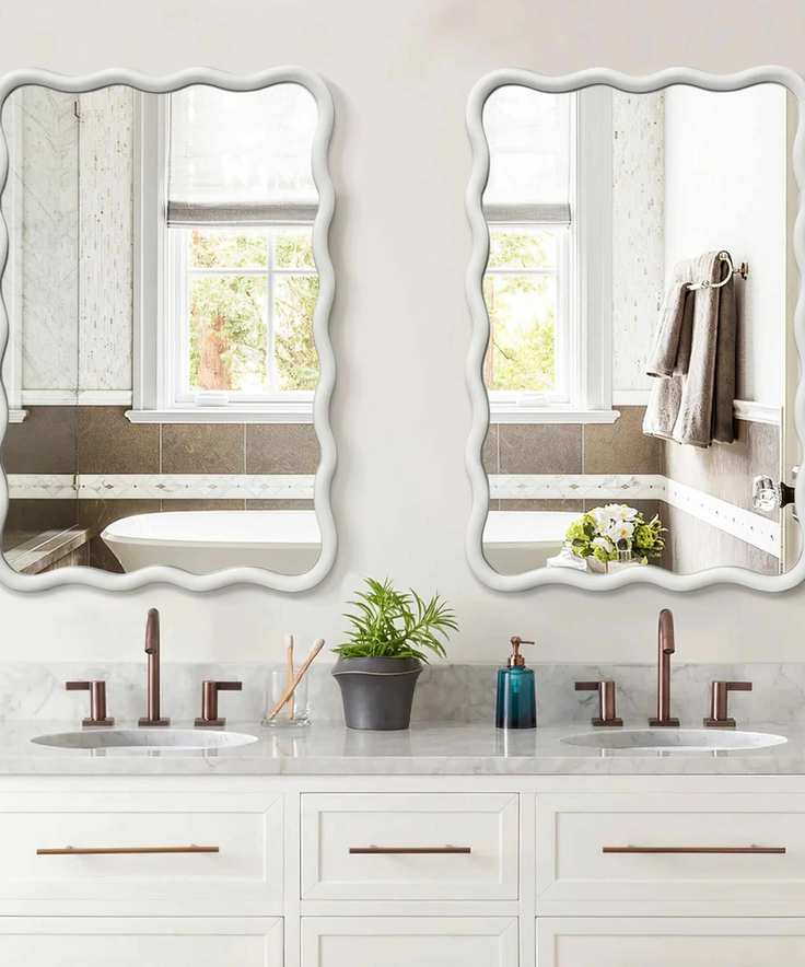 A white bathroom with wavy vanity mirrors and bronze faucets