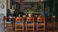 a dining area with vintage swedish pine chairs looking through to an open plan dark green kitchen
