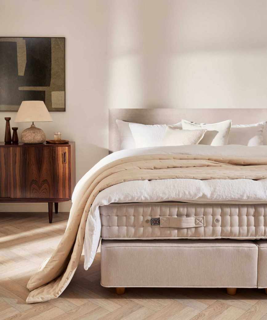 neutral bedroom with an unmade bed showing the mattress, duvet, and pillows with a linen bed frame and mid century room decor