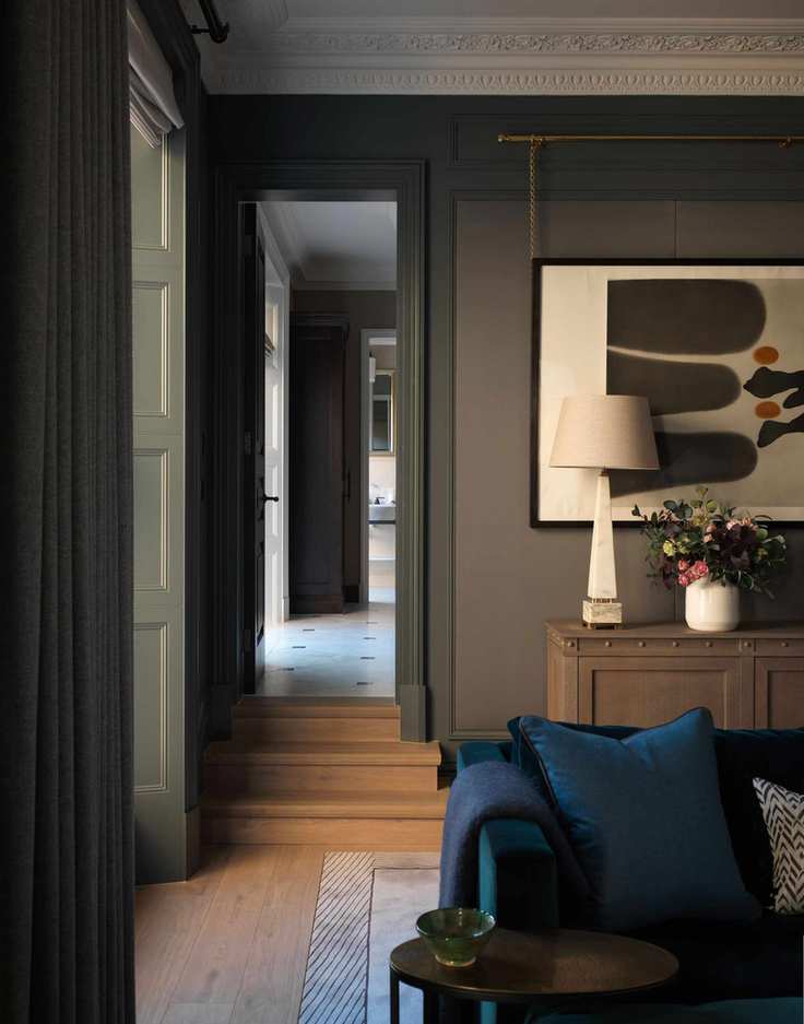 dark painted living room with light coloured modern painting, lamp and vase, blue sofa and cushions, wooden floor