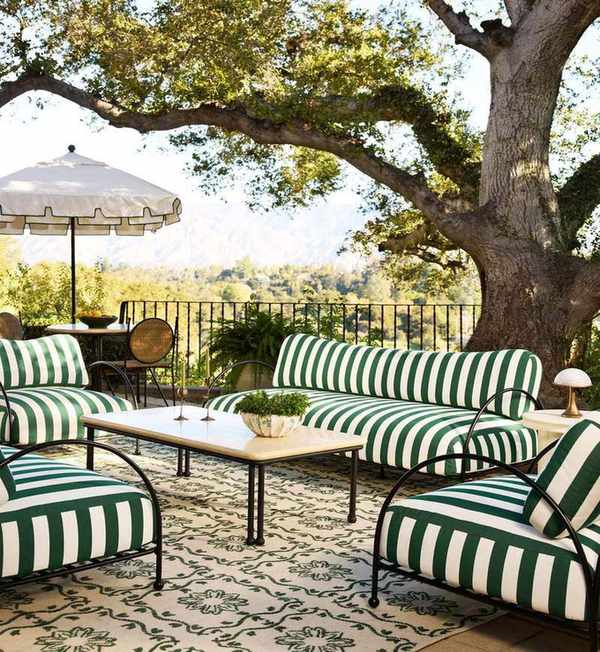 a european style terrace with a large tree, and an arrangement of green striped wrought iron furniture on a patterned green floral rug