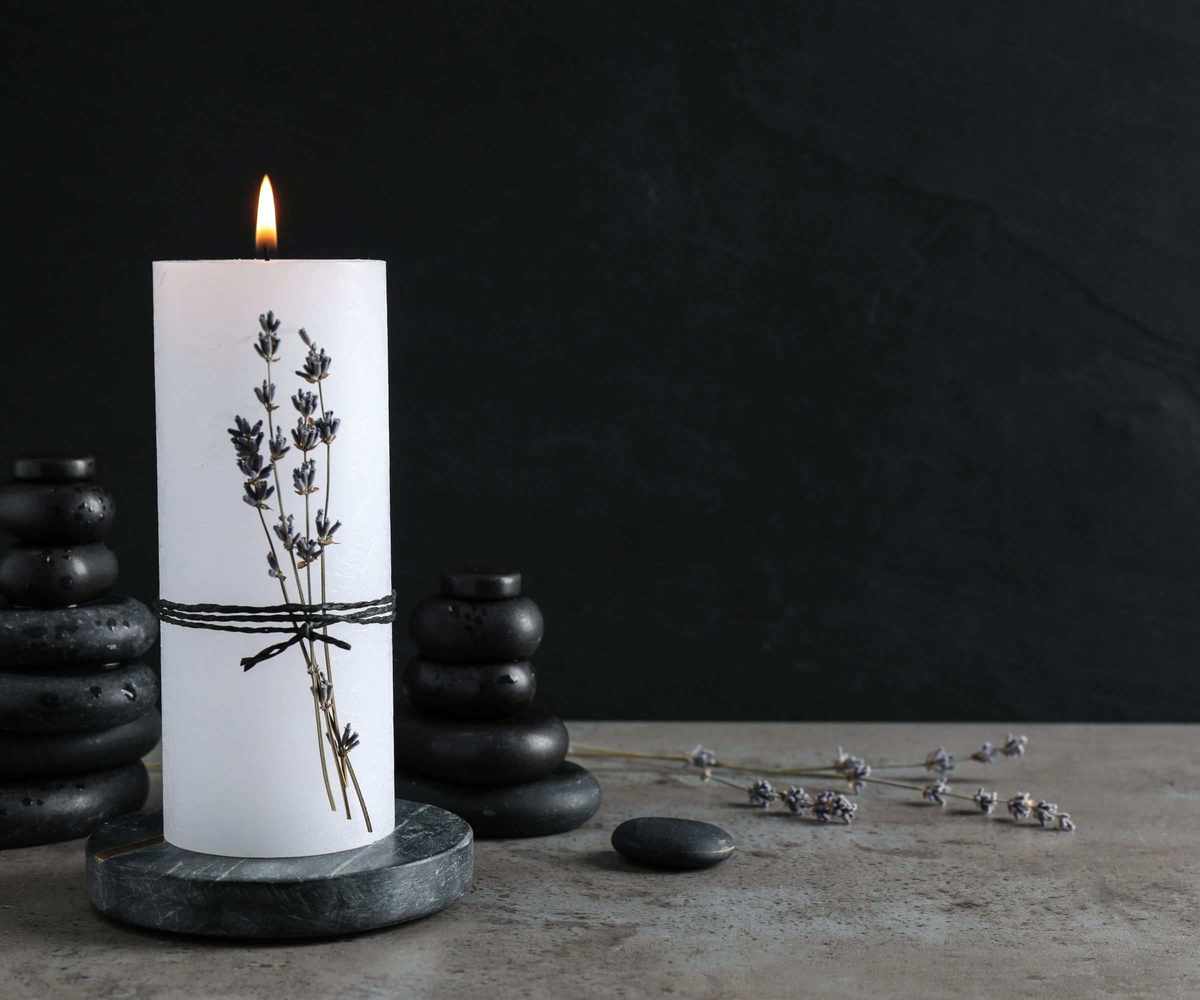 A single candle with lavender wrapped around it and smooth dark stones