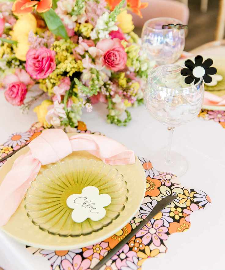 bright pink and orange themed tablescape with bold floral placemats, yellow plates, pink napkins and colorful flowers