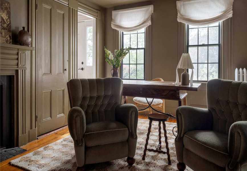 Muted earthy green living room with velvet armchairs, wooden floor, a desk and a chequered rug