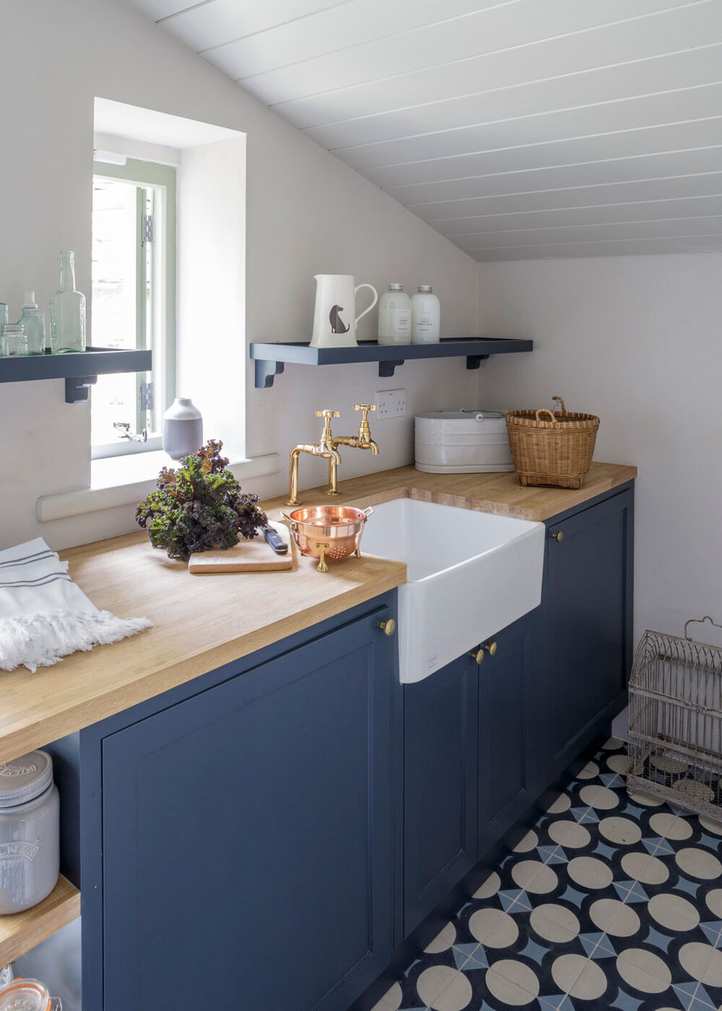 Compact laundry room under a sloped ceiling featuring blue cabinetry and open shelves.