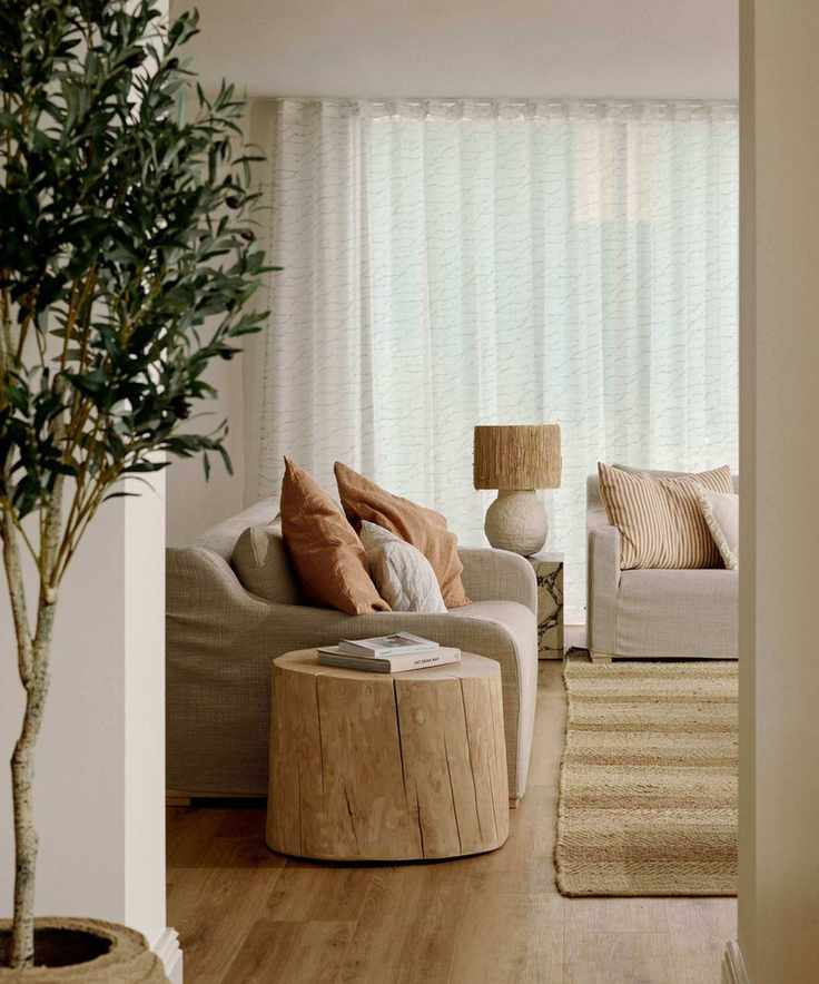 neutral warm minimalist living room with a jute rug, two linen slip covered sofas, a rustic wooden side table and an olive tree