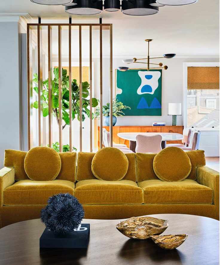 a white living room with wooden dividers, wooden coffee table, mustard velvet couches and abstract art and decor