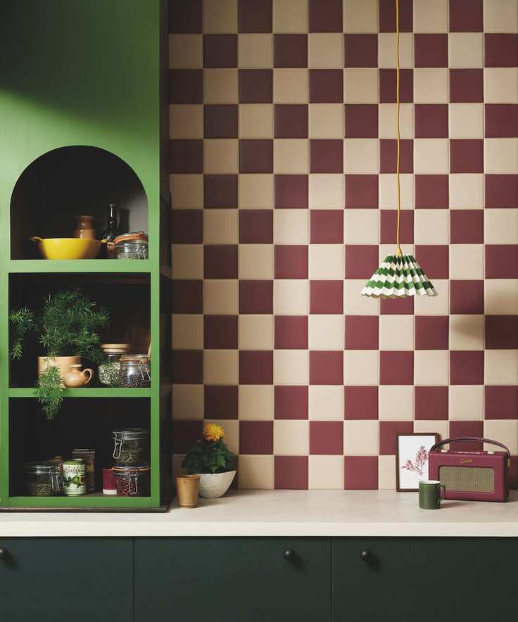 A small kitchen with dark green cabinets, a bold green shelf, and white and merlot checkerboard backsplash tiles