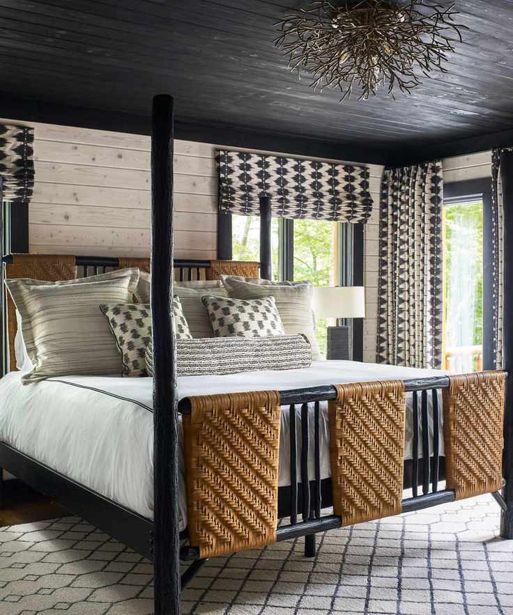 White sheets and gray pillows on a black and rattan bed base against a white wall and a black ceiling.