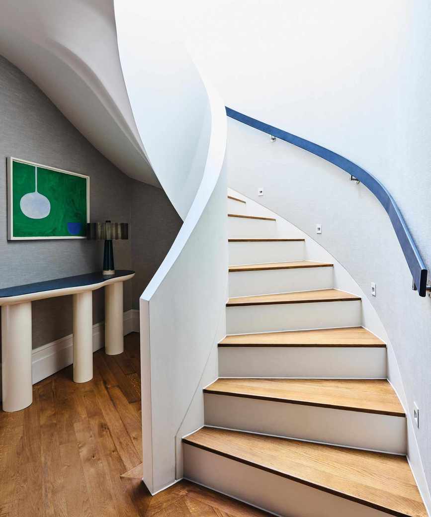 a white curved staircase with wooden treads, a blue curved handrail and a white and blue sculptural hall table