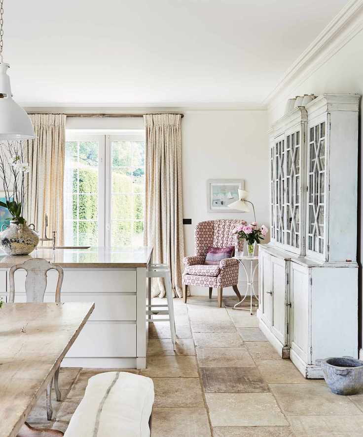 A large kitchen with stone flooring, a white island and a large kitchen dresser next to an armchair