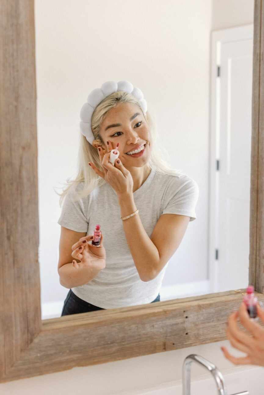 Woman treating puffy eyes in mirror.
