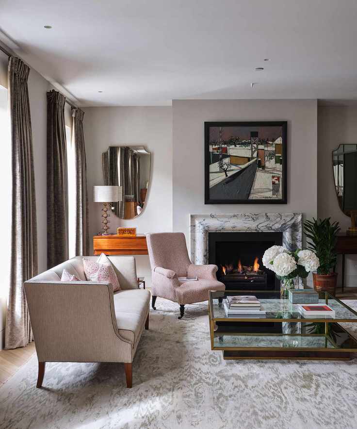 A stylish living room painted with a mid gray-beige, with mirrors and spotlights and a glass coffee table in front of a fireplace.