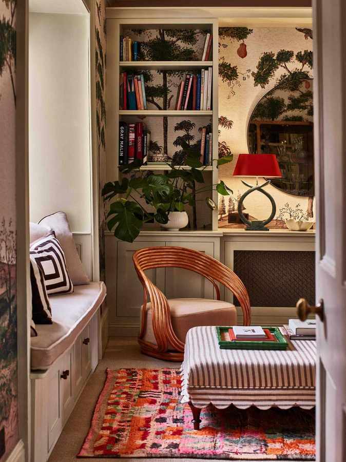 cozy snug room with mural wallpaper and neutral bookshelves styled with a red table lamp, window seat nook with a striped ottoman with scalloped trim