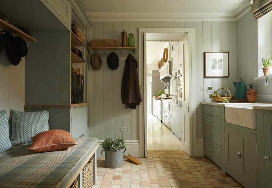 A large mudroom with a tartan bench, a sink area to the right and a doorway into the kitchen in the background