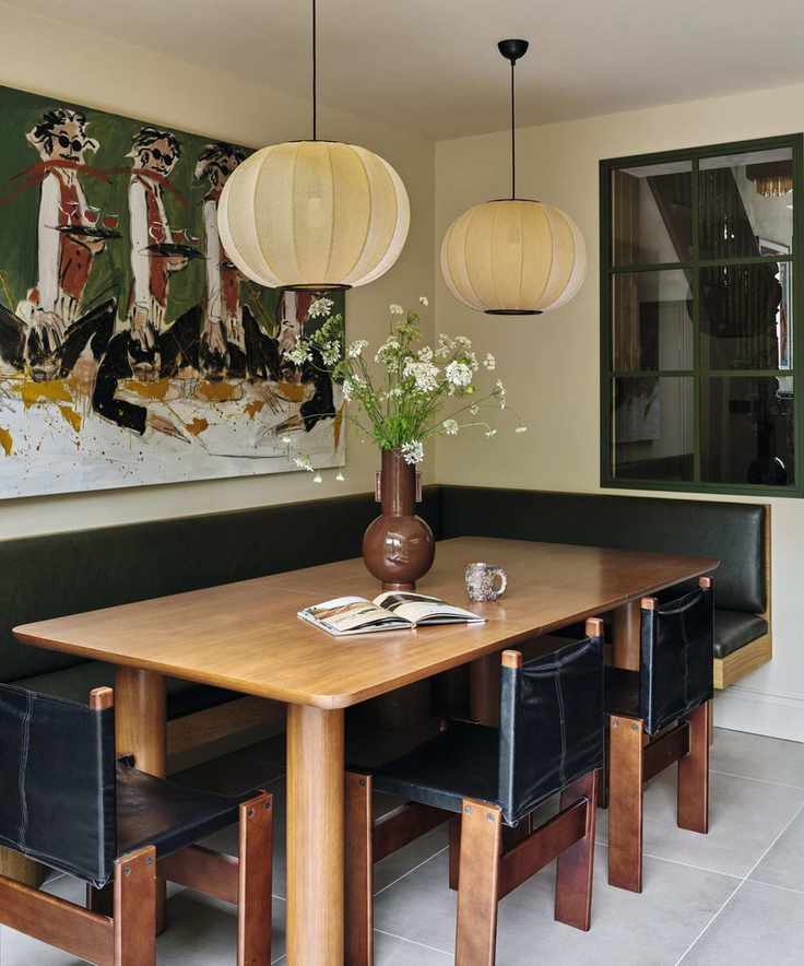 a modern meets vintage dining nook in a Victorian home with a black leather banquette, wooden table and vintage wood and leather chairs with large painted art on the wall