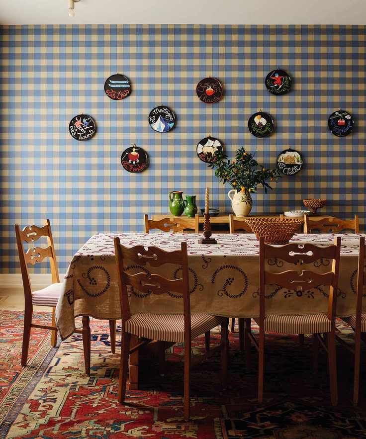 a dining room with blue plaid wallpaper, wall plates, a vintage pine dining table and chairs and a vintage red rug