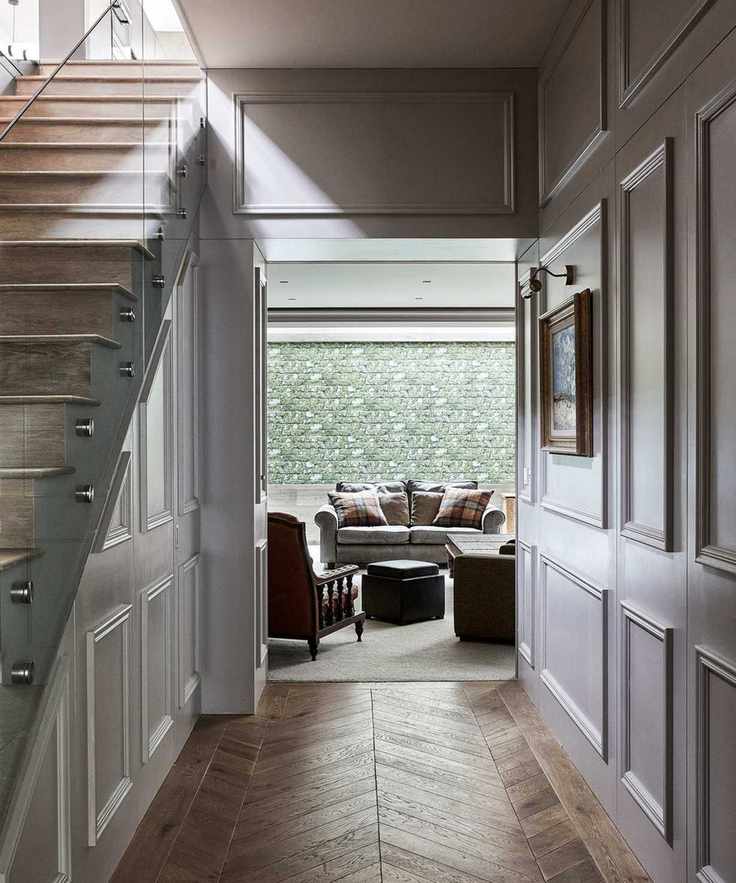 Small hallway design featuring herringbone flooring and light gray wood paneling looking toward a living area.