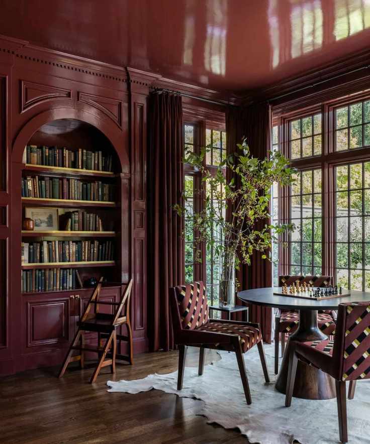 a study room with red lacquered walls and ceiling, a round table with a chess board, a built-in bookshelf, and several chairs