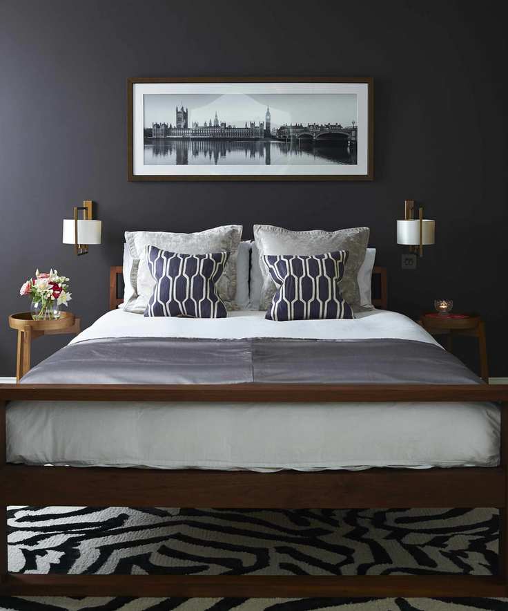 A black bedroom with a wooden bed, white linen and a black and white striped rug