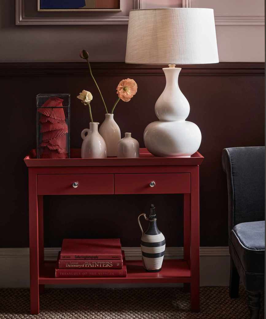 red console table in a hallway with dark red walls below dado and dusky pink above