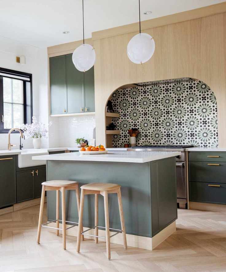 Scandi style kitchen in sage green and blond wood, tiled backsplash, kitchen island, white pendant lights, bar stools, herringbone floor