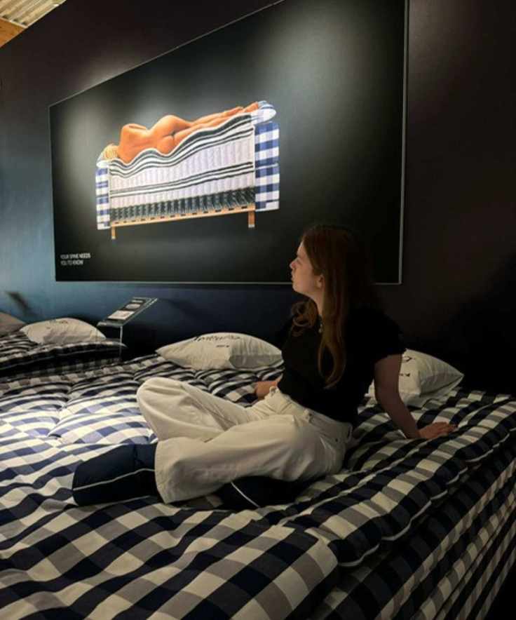 Emilia on a Hästens mattress with a spinal alignment poster.