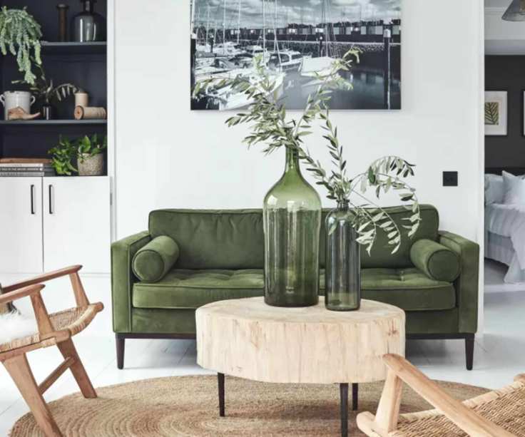 A white living room with a green sofa and natural wood chairs