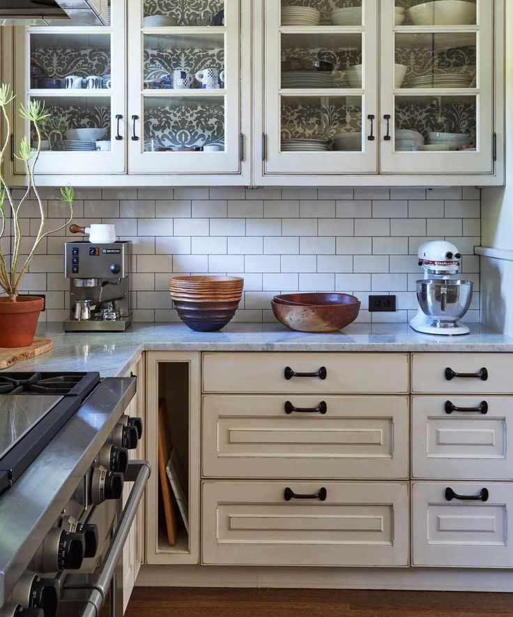 A white kitchen with glass-fronted cabinets and iron vintage kitchen hardware
