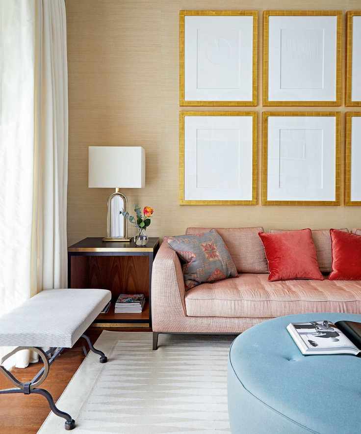 Living room with wallpapered wall, elaborate cornice, red sofa and large circular ottoman.