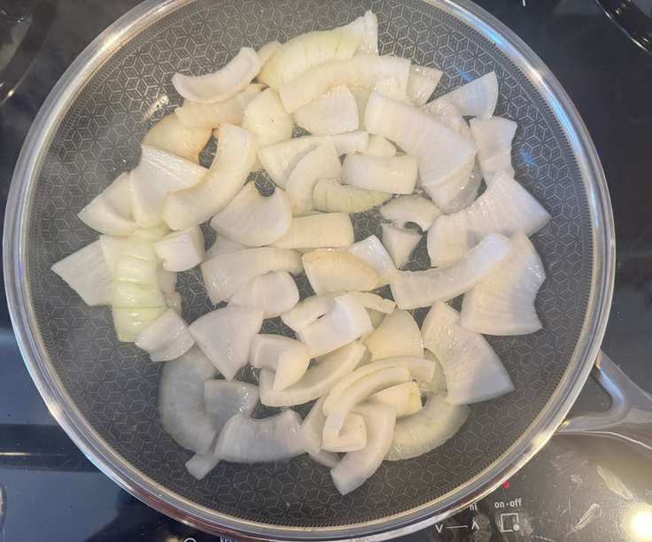Chopped onions in a black-lined stainless steel frying pan on a black induction stove.