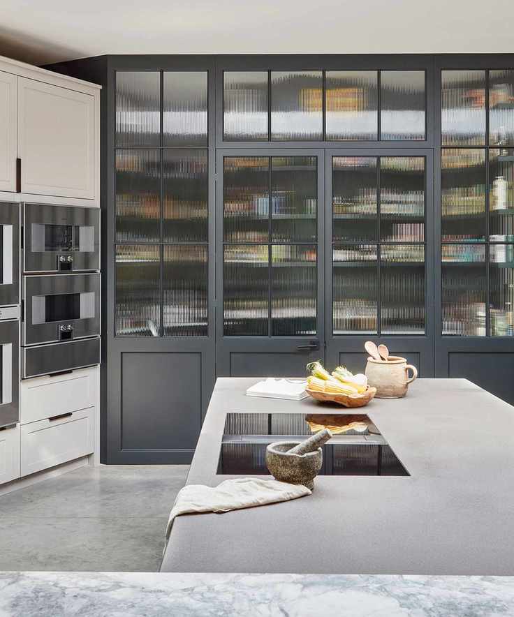 Modern pantry with glazed cabinet doors and stone surface