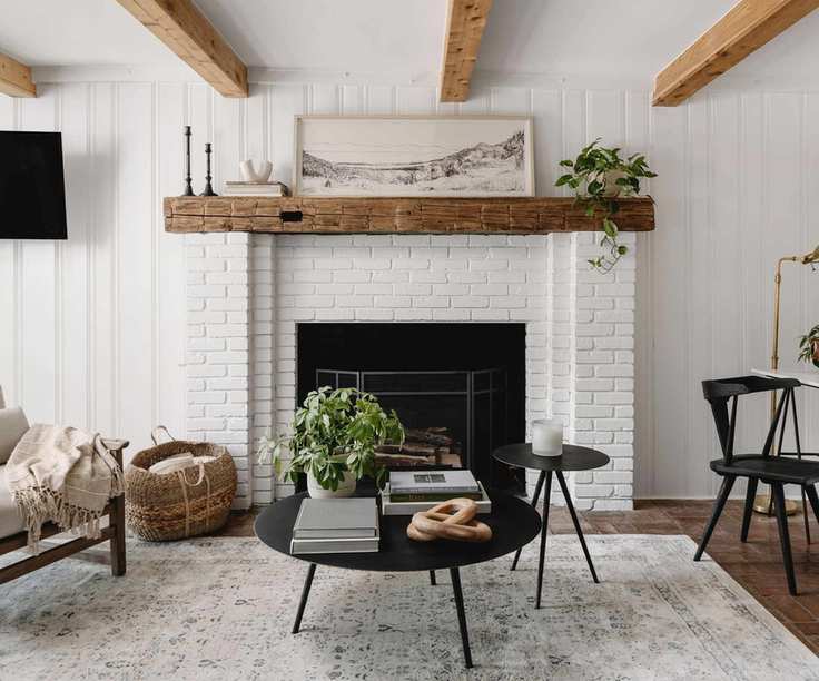 Cottage fireplace with exposed brick, beams, black round coffee table with books and plant and basket