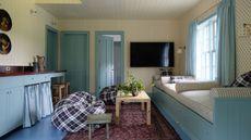 a small open plan cottage with light blue painted door trims, small kitchenette, banquette seating and a ditsy floral wallpaper on the walls
