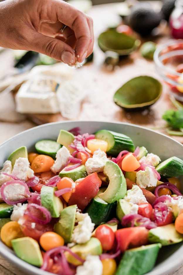 sprinkling cheese on tomato, avocado, and cucumber salad