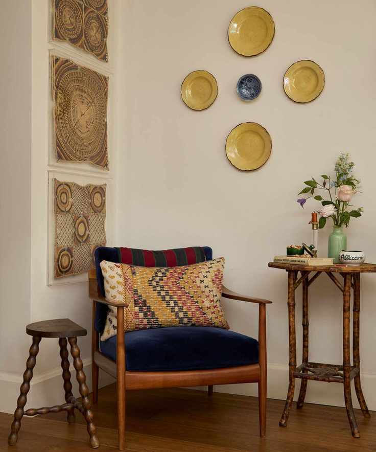 Eclectic hallway with vintage ceramic plates on wall, wood armchair and side table with antique wall hangings