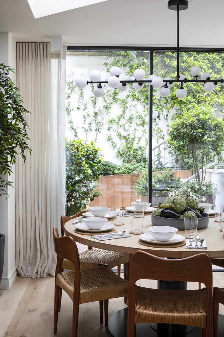 dining room with globe pendant light, retro round table and chairs, large glass doors with view of garden
