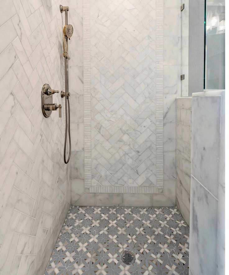 A tiled shower with brass hardware and marble half wall with glass screen
