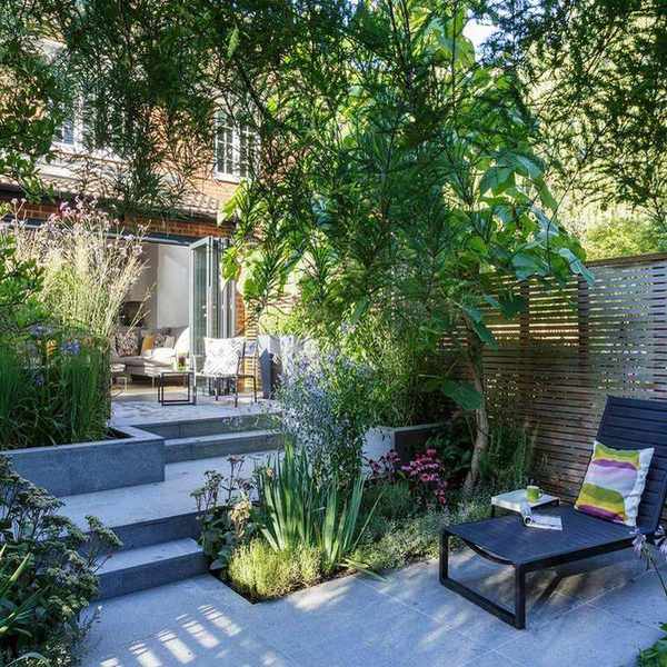 Small garden ideas with a stone patio and steps surrounded by green leafy vegetation and a wooden fence.