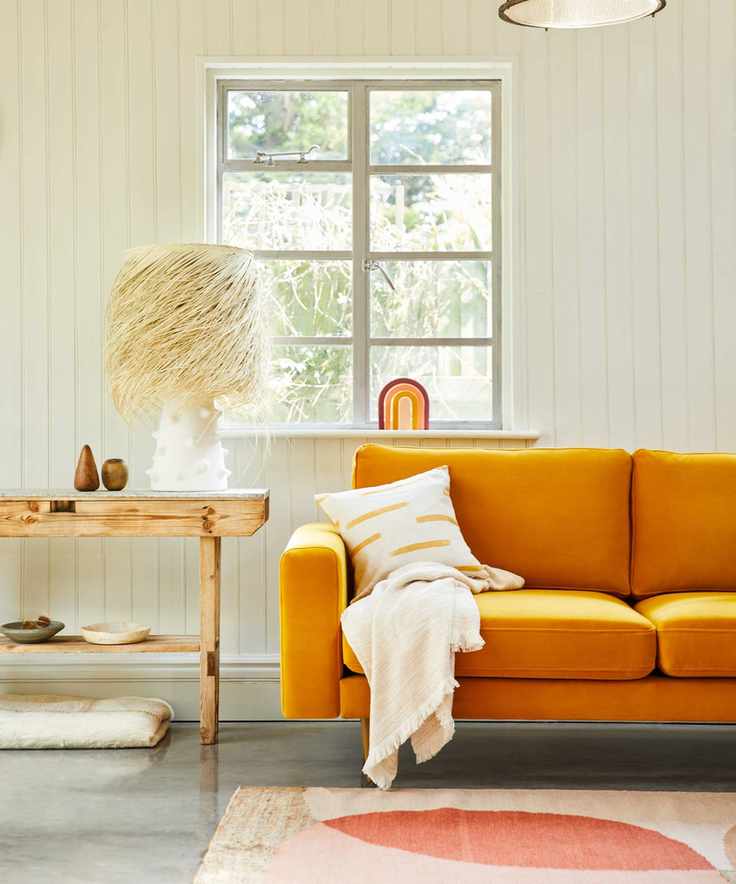 A living room with a turmeric yellow sofa set against a white paneled wall