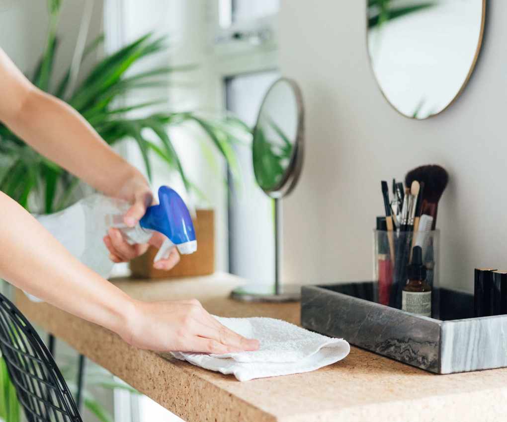 A lady using a cloth and spray to wipe down a makeup desk