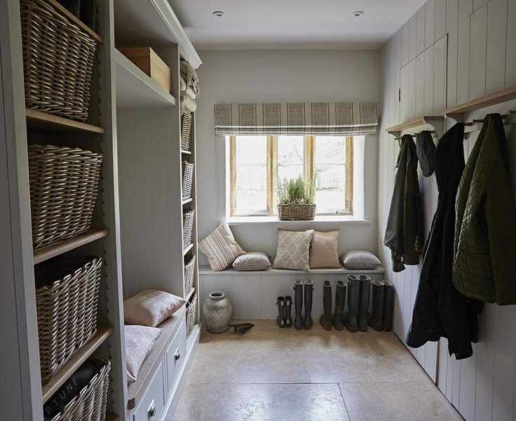 An example of mudroom ideas showing a mudroom with bench seating with cushions below a window and wall storage and coat hooks