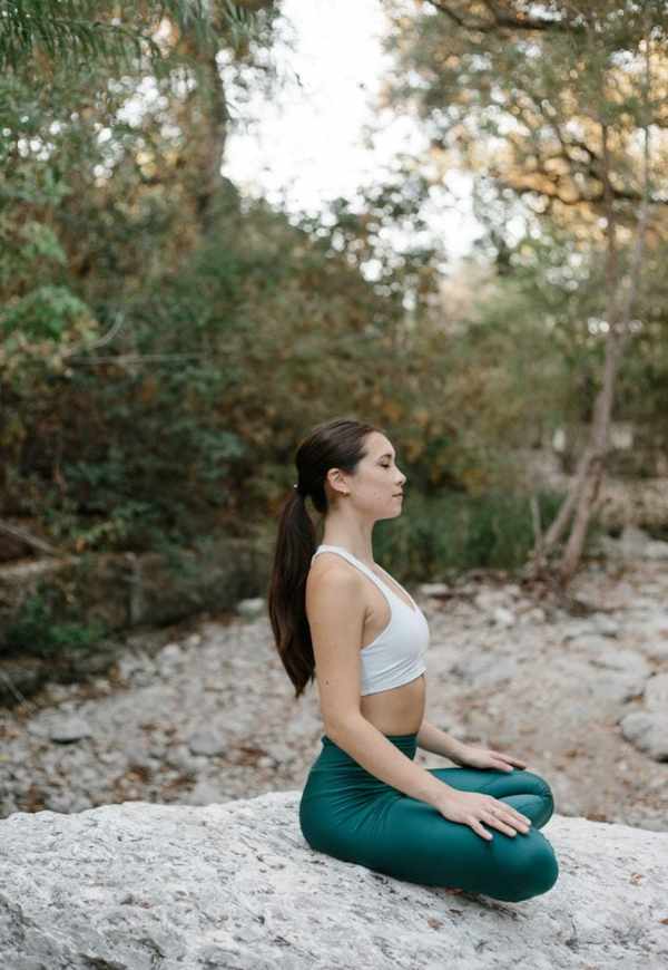 Woman meditating on rock outside.